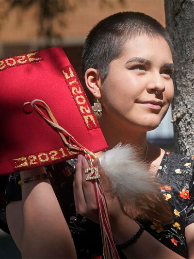 Emalyce Kee, holding up her "forbidden" graduation cap that she decorated with Native beads on May 25, 2022, in Cedar City, Utah.
