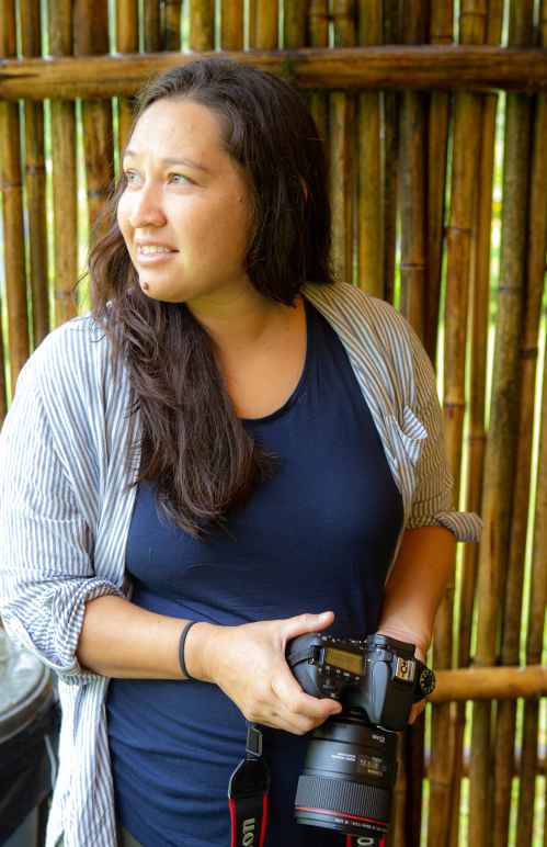 Portrait shot of communications director Kimberly Moa holding a DSLR camera and looking into the distance