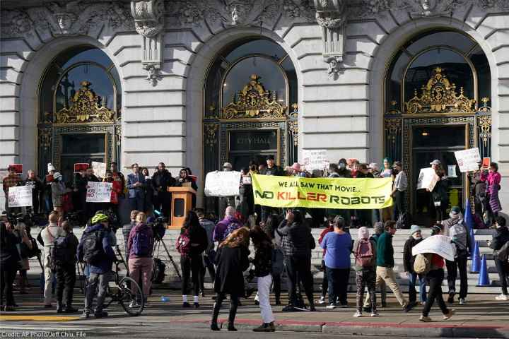 Demonstrators, (holding various signs, with the most prominent reading "WE ALL SAW THAT MOVIE ... NO KILLER ROBOTS") protest the use of robots by the San Francisco Police Department outside of City Hall in San Francisco, Monday, Dec. 5, 2022.