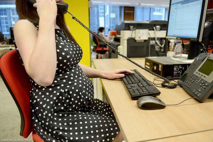 A pregnant worker using an office phone while typing on a keyboard.